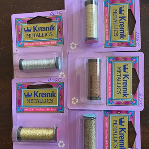 May include: Five spools of Kreinik metallic thread in various colors, including gold, silver, and bronze. Each spool is labeled "Kreinik Metallics" and "Balger Very Fine (#4) Braid".