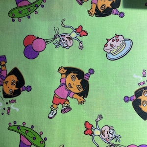 May include: Light green fabric featuring a repeating pattern of Dora the Explorer and Boots characters. The design includes Dora in a party hat, a cake, balloons, and a sombrero. The fabric is suitable for children's crafts and apparel.
