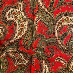 Può includere: Tessuto rosso con un motivo paisley in tonalità di verde, crema e nero.