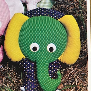 Puede incluir: Un juguete de peluche de elefante verde y amarillo con tela de lunares negros y blancos en las patas y la trompa. El elefante tiene ojos grandes blancos y una pequeña nariz rosa.