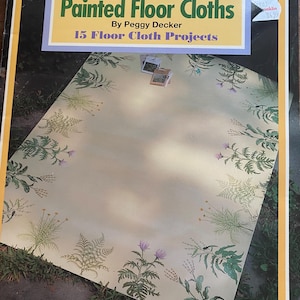 Könnte beinhalten: Ein Buch mit dem Titel "Painted Floor Cloths" von Peggy Decker. Das Cover zeigt ein Design für einen bemalten Canvas-Teppich mit Blumen- und Pflanzenillustrationen. Das Buch gehört zur Reihe "How-To Create A Painted Canvas Rug".