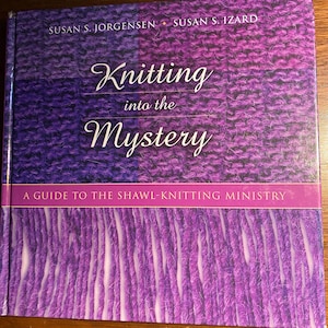 May include: A book titled "Knitting into the Mystery" with a purple and violet knitted texture design. The cover features the names Susan S. Jorgensen and Susan S. Izard. The subtitle reads "A Guide to the Shawl-Knitting Ministry."
