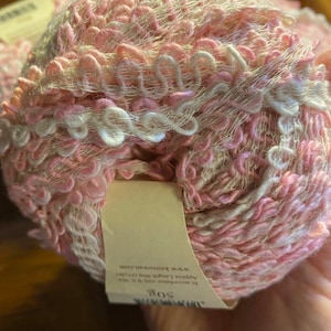 Pode incluir: Um novelo de fio rosa e branco com um rótulo que diz "Soft", "Approx Length 300g (10.5 oz)" e "www.knitrowan.com".
