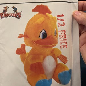 May include: A plush orange Firefells character toy with blue feet and a white belly. The toy has a red crest and wings. The image is on a pattern with the text "crafts/ouvrages" and "1/2 PRICE".