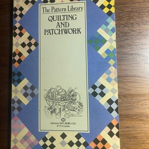 May include: A book titled "The Pattern Library Quilting and Patchwork" with a blue cover and a patchwork design. The cover features a central white rectangle with text and an illustration of sewing supplies. The book is a guide for quilting and patchwork.