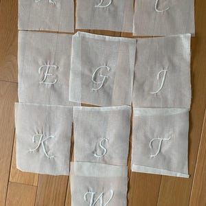 May include: Ten white fabric squares with embroidered letters, A through W, in a cursive font.