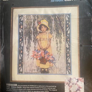 May include: A Dimensions no count cross stitch kit featuring a portrait of a girl in a yellow dress and hat, holding a basket of flowers. The kit includes the text "REBECCA" and instructions for cross-stitch.