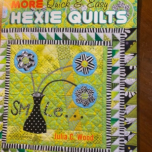 May include: Book cover featuring a colorful quilt with a vase of flowers and the words "Smile" and "More Quick & Easy Hexie Quilts". The book is by Julia C. Wood and published by AQS Publishing.