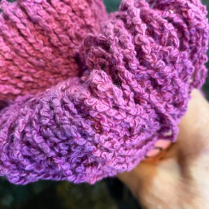 May include: A close-up of a purple yarn ball. The yarn is soft and fluffy, and it is perfect for knitting or crocheting.