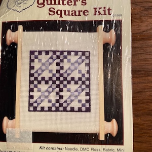 Könnte beinhalten: Ein Kreuzstich-Set mit einem Holz-Rollrahmen. Das Set enthält eine Nadel, DMC-Garn, Stoff und Anleitungen. Das Design heißt "Flying Clouds" und ist Teil der Serie "Quilter's Square Kit". Das Set ist von Cross My Heart, Inc. und ist urheberrechtlich geschützt 1989.