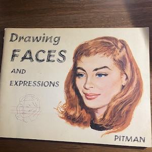 May include: A rectangular instructional book titled Drawing Faces and Expressions by Pitman. The cover features a painted portrait of a person with auburn hair and blue eyes, alongside a simple black line drawing showing facial construction lines.