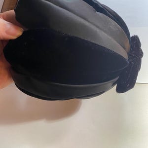 May include: A black velvet hat with a large bow on the side.