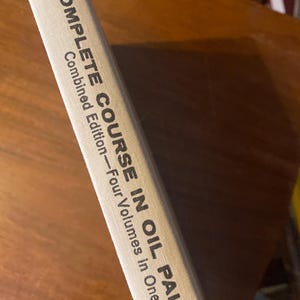 May include: A close-up of a book spine with the title "COMPLETE COURSE IN OIL PAINTING" in black text on a light beige cover. The book is a combined edition of four volumes in one.