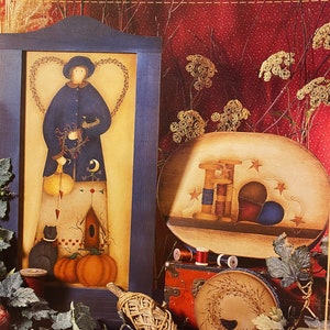 May include: A painting of a woman holding a bird in a blue dress with a heart-shaped wreath around her head. The painting is in a blue frame and is next to a painting of a spool of thread with a heart-shaped patch. The text "Kindred Hearts 2" and "By Viki Sherman" is on the top of the image.