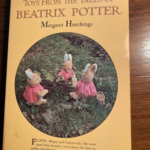 May include: A book titled Toys From The Tales of Beatrix Potter by Margaret Hutchings. The cover is yellow with a circular image of three plush rabbits wearing pink capes in a grassy area. Text at the bottom reads Flopsy, Mopsy and Cotton-tail.