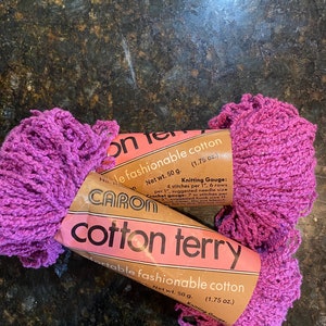 May include: Two skeins of Caron Cotton Terry yarn in a bright pink color. The yarn is packaged in brown paper with the brand name Caron and the yarn name Cotton Terry. The label also includes the weight of the yarn, 1.75 ounces, and the knitting gauge.