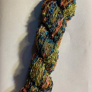 May include: A skein of yarn with a multi-coloured, textured, and sparkly appearance. The yarn is a mix of green, blue, brown, and pink.