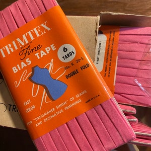 May include: A package of pink bias tape labeled "Trimtex Fine Bias Tape" with the text "6 Yards No. K 20-5 Double Fold" and "Fast Color For "Dressmaker Finish" of Seams and Decorative Trimming Made in U.S.A."