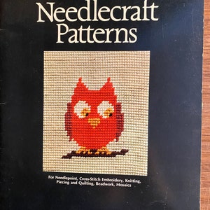 Op de afbeelding: Een boekomslag met de titel "Needlecraft Patterns" in grote, vetgedrukte letters. De omslag toont een rode uil met witte ogen en een gele snavel, gestikt in kruissteek. Het boek is voor naaldkunst, kruissteekborduren, breien, patchwork en quilten, kralenwerk en mozaïeken.