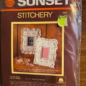 May include: A cross-stitch kit for a 5" x 7" photo frame featuring a design of tulips and lace. The kit includes cotton fabric, embroidery floss, lace, tracing cloth, batting, a needle, and instructions. The kit is labeled "Sunset Stitchery" and "890".