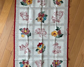 Könnte beinhalten: Ein weißes Stoffpanel mit rotem Rand zeigt ein sich wiederholendes Muster aus roten Hähnen, gelben Blumen und roten Äpfeln. Der Stoff ist für Quilten oder andere Bastelarbeiten gedacht.