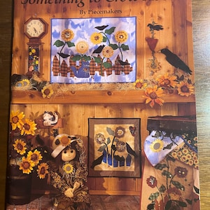 May include: A book titled "Something to Crow About" by Piecemakers, featuring a quilt design with crows, sunflowers, and a fence. The book cover shows a rustic setting with a doll, a clock, and other decorative elements.