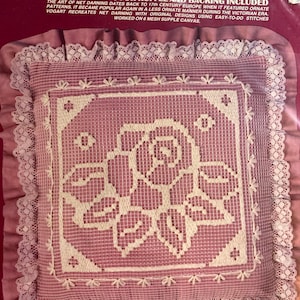 May include: A pink net darning kit by Vogart Crafts. The kit includes lace and fabric for a ruffle and backing. The kit features a pink and white floral design with a lace border. The text on the package reads "Net Darning Kit".