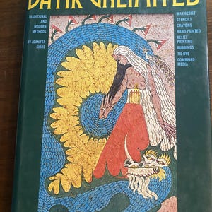 Könnte beinhalten: Ein gebundenes Buch mit dem Titel Batik Unlimited von Joanifer Gibbs mit dunkelgrünem Einband. Die Vorderseite zeigt eine farbenfrohe Illustration einer Figur mit langem weißem Haar und einem drachenartigen Wesen. Text listet Methoden auf.