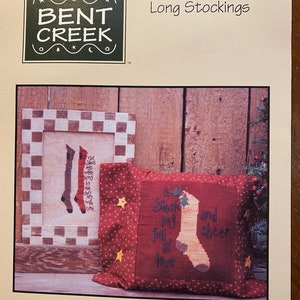 May include: A product image featuring a cross-stitch design with the text "Long Stockings." The image includes a framed cross-stitch of stockings and a pillow with a stocking design and the words "A Stocking full of love and cheer."