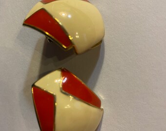 May include: A pair of clip-on earrings with a geometric design. The earrings are made of gold-tone metal and have a white and red enamel finish.