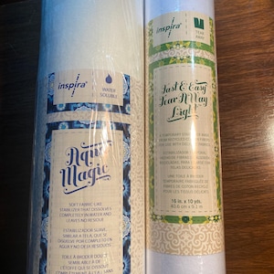 May include: Two rolls of white water-soluble fabric stabilizer. The roll on the left is labeled "Aqua Magic" and has instructions for use in English and Spanish. The roll on the right is labeled "Fast & Easy Tear Away Light" and has instructions for use in English and French. Both rolls are 16 inches wide.