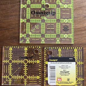 Op de afbeelding: Drie vierkante Omnigrid quiltlinialen van transparant geel en zwart acryl. De grootste liniaal is gemarkeerd met RN35, terwijl de twee kleinere linialen gemarkeerd zijn met R25G en 6,35 cm bij 6,35 cm meten. Elke liniaal heeft rasterlijnen.