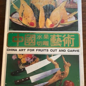 Può includere: Un libro intitolato "China Art for Fruits Cut and Carve" con testo cinese e inglese. La copertina presenta composizioni di frutta intagliata, coltelli e una mela. Il tema del libro sono le tecniche di intaglio della frutta.