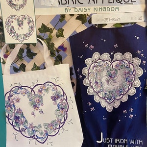 Puede incluir: Kit de aplique de tela sin coser con un diseño en forma de corazón con flores moradas y hojas verdes. El kit incluye instrucciones para usar tela fusible y pintura lisa para crear un proyecto terminado. El kit es de Daisy Kingdom y tiene el SKU #257-8524.