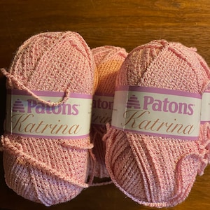 May include: Three balls of pink Patons Katrina yarn. The yarn is a soft, textured yarn with a subtle shimmer.