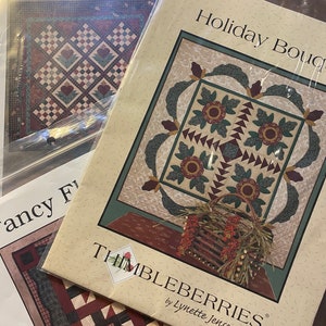 May include: Three quilting patterns featuring holiday themes. The patterns are titled "Blossom Five-Patch", "Holiday Bouquet", and "Fancy Five Patch". The patterns are printed on cream-coloured paper with a brown and green floral design.