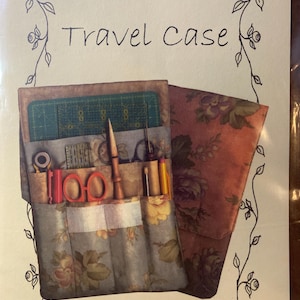 May include: A floral-patterned travel case with the words "Travel Case" in black script. The case is open, revealing sewing tools, including scissors, a ruler, and a needle. The case is decorated with a floral design.