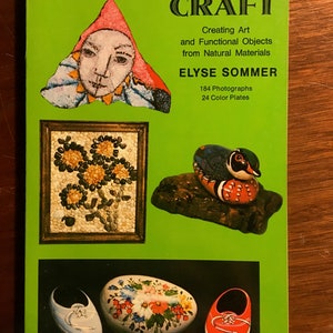 May include: Book cover with the title "Rock and Stone Craft: Creating Art and Functional Objects from Natural Materials" by Elyse Sommer. The cover features a green background with images of rock crafts, including a painted face, a mosaic flower arrangement, a painted duck, and a painted shoe.