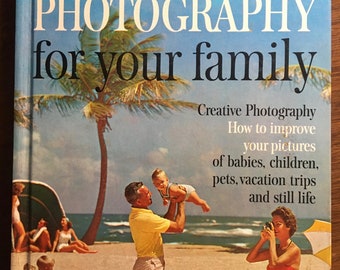 Pode incluir: Um livro intitulado "Better Homes & Gardens Fotografia para sua família" com uma imagem de capa de uma família numa praia. A família é composta por um homem que segura uma criança pequena no ar, uma mulher que tira uma foto e duas crianças sentadas na areia. A capa do livro também inclui o texto "Fotografia criativa, Como melhorar suas fotos de bebês, crianças, animais de estimação, viagens de férias e naturezas mortas."