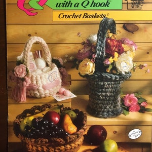 May include: A crochet pattern book cover featuring three crocheted baskets. The baskets are filled with fruit, flowers, and other items. The book cover is titled "Quick & Easy with a Q hook Crochet Baskets".