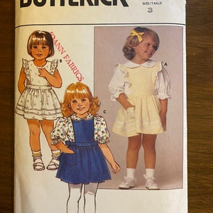 Puede incluir: Un patrón de costura vintage para un vestido de niña. El patrón es para la talla 3 y es de Butterick, número de patrón 6584. El patrón incluye tres estilos diferentes de vestidos, todos con un cuello Peter Pan y un ribete de volantes.