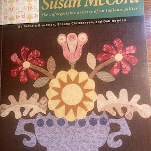 Puede incluir: Portada de libro con un diseño de colcha colorido de un jarrón con flores. El título es "Our Favorite Quiltmakers Susan McCord" y el subtítulo es "The unforgettable artistry of an Indiana quilter". Los autores son Barbara Brackman, Shauna Christensen y Deb Rowden.