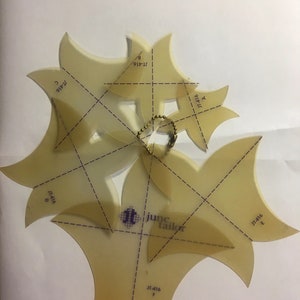 Könnte beinhalten: Sechs transparente Nähschablonen aus Kunststoff mit einem Rastermuster und dem aufgedruckten Text "JT-416" und "june tailor". Die Schablonen sind in Form von Blütenblättern geformt und durch einen Metallring verbunden.
