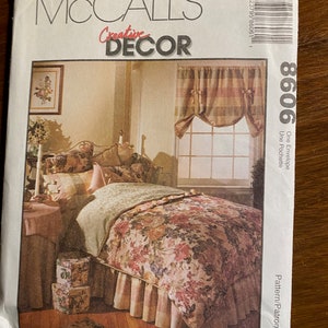 May include: McCall's Creative Decor sewing pattern number 8606. The pattern includes instructions for making a bed skirt, a bedspread, and a window valance. The image shows a bed with a floral bedspread and a ruffled bed skirt. The window valance is a plaid fabric with a gathered design.