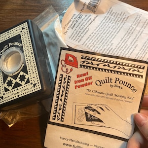 May include: Quilt Pounce by Hancy, a quilting tool with a black and white design. The packaging features a hand using the tool with the text "New! Iron Off Powder" and "The Ultimate Quilt Marking Tool. Now with iron-off Ultimate Pounce Powder!" The packaging also includes the website address www.fulllinestencil.com.
