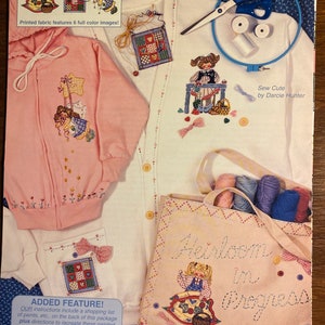 May include: A craft kit featuring applique designs for a pink hooded sweatshirt, a white cardigan, and a beige tote bag. The designs include a girl swinging on a swing, a girl sewing, and a girl sitting on a quilt. The kit includes instructions and a shopping list of paints.