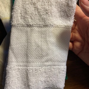 Puede incluir: Primer plano de una toalla de mano blanca con una secci&oacute;n superior de rizo texturizado y una secci&oacute;n inferior tejida. La toalla tiene flecos en la parte inferior y un borde tejido. La toalla est&aacute; limpia y parece sin usar.