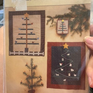 May include: A vintage craft pattern for making three different Christmas tree wall hangings. The pattern includes instructions for a tree with birds, a tree with ornaments, and a tree with a snowman and other winter characters. The pattern is titled "Feather Tree" and is numbered #153. The pattern also includes a small image of a miniature Christmas tree with lights.
