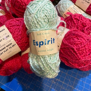 Op de afbeelding: Twee bollen garen, een roze en een lichtblauw. De lichtblauwe bol is gelabeld "Soft Cotton Espirit worsted weight".