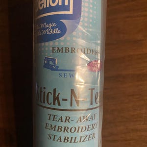 May include: A roll of Pellon Stick-N-Tear tear-away embroidery stabilizer in light blue packaging. The label features the text The Magic in the Middle, Embroider, Sew, and Stick-N-Tear, along with a small graphic of a sewing machine.